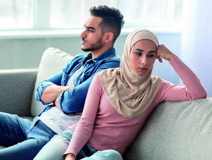 Sad young woman in hijab sitting by her sad husband