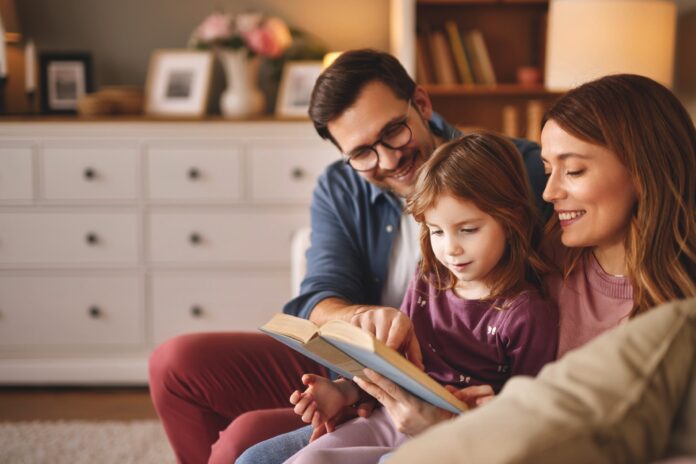 Family with little daughter reading book on sofa in living room