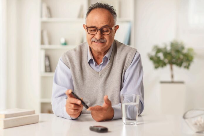 Mature man sitting at home and checking blood sugar level with glucose meter
