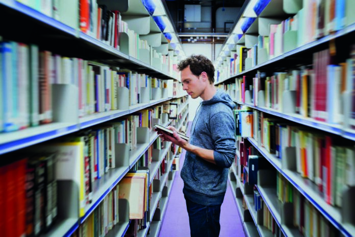 Young,Student,Reading,Book,Between,The,Shelves,In,The,Library